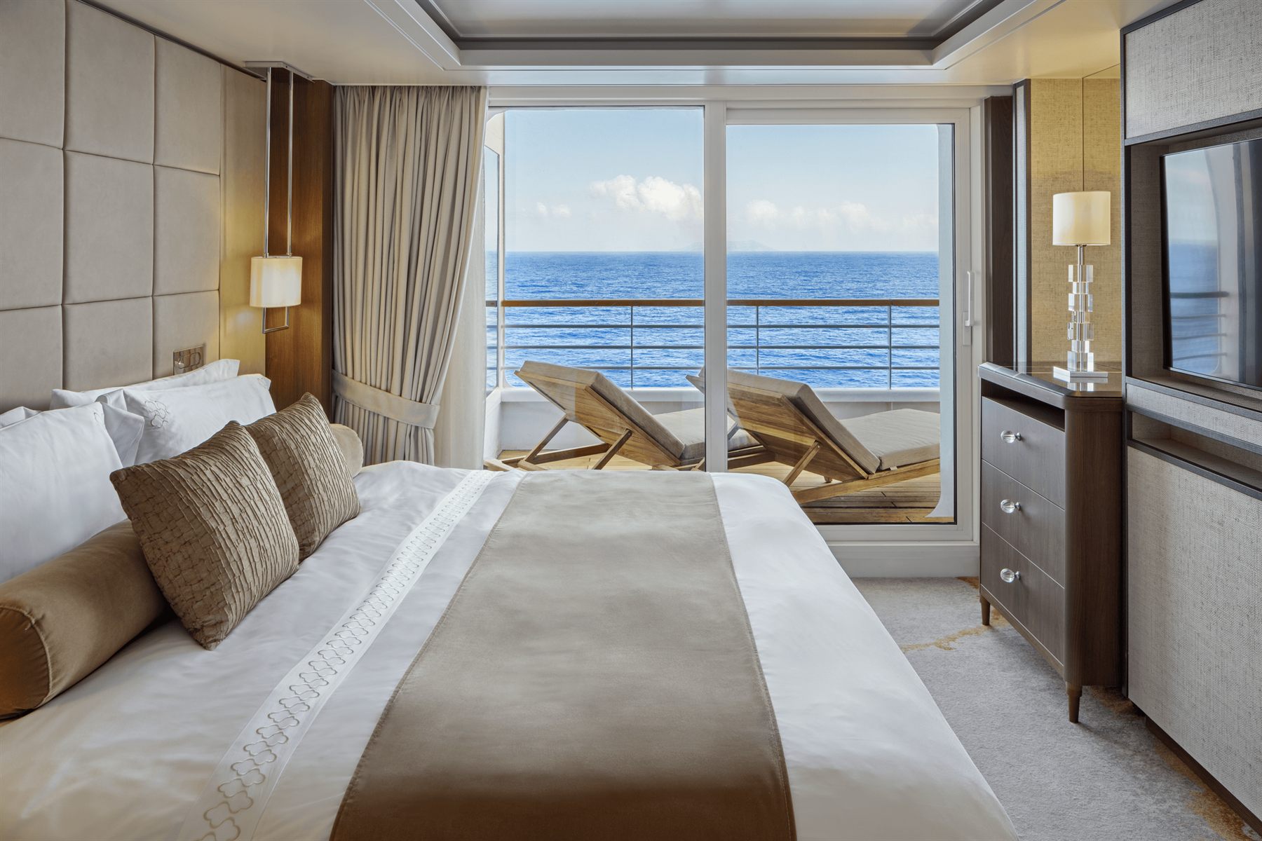 A luxury suite bedroom opening onto a private balcony with loungers and an ocean view